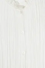 Blusa de cuello redondo con detalle de volados, manga corta abullonada con terminación elástica y cierre frontal con botones. Presenta un diseño de tejido plisado en toda la prenda.