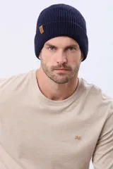 Gorro tejido de punto acanalado en color azul marino, con vuelta y etiqueta decorativa de cuero sintético en el lateral.