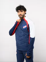 Buzo de entrenamiento Umbro del Club Nacional de Football, con cierre frontal parcial y cuello alto. Presenta un diseño con bloques de color azul, blanco y rojo, con panel frontal acolchado y mangas largas con aberturas para pulgares.