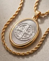 Collar de cadena de eslabones con baño de oro y dije ovalado colgante con relieve de San Benito en tono plateado y borde dorado.