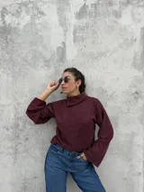 Polera de punto color bordó, con cuello alto abierto lateralmente, mangas largas amplias y corte recto.