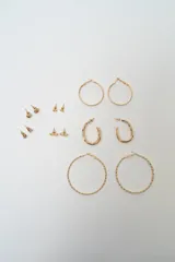 Set de siete pares de aros dorados de diversos estilos, incluyendo aros de argolla lisos, argollas texturadas, aros ovalados y aros pequeños tipo broche con diferentes formas.