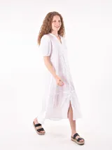 Vestido midi de broderie color blanco, con cuello mao y escote en V, cierre frontal con botones, mangas cortas abullonadas y detalle de volado en el ruedo.