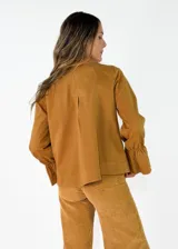 Chaqueta color tostado de corte recto y diseño cruzado con doble botonadura frontal. Presenta cuello solapa y mangas largas con puños acampanados y fruncidos.