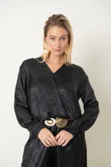 Blusa negra laminada con escote en V cruzado, mangas largas y elástico en la cintura.