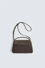 Bolso tipo bandolera fabricado en piel con acabado serraje. Cuenta con compartimento principal con cierre de solapa magnética y cremallera, asa de mano superior y asa de hombro ajustable.