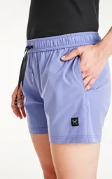 Short de baño de calce regular, color lavanda, con cintura elástica ajustable mediante cordón negro. Posee bolsillos laterales y un pequeño parche negro con un logo de tijeras cruzadas en la parte inferior frontal.