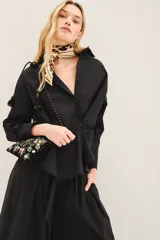 Camisa de popelina de algodón en color negro, con corte amplio, cuello clásico y cierre frontal con botones. Presenta un diseño versátil con botones en los laterales que permiten un ajuste cruzado.