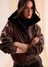 Chaqueta estilo bomber de cuero color marrón con efecto desgastado vintage, corte amplio a la cintura, mangas caídas y aplique de corderito negro en el cuello y el interior delantero.