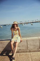 Vestido corto blanco con estampado de bananas, limones, piñas y sombrillas. Tiene breteles finos ajustables, escote corazón y cuerpo entallado con frunces en el escote y laterales. La falda es levemente acampanada.