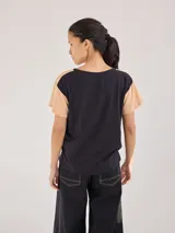Remera de algodón con diseño bicolor, cuerpo en color negro y mangas en color beige. Presenta un detalle de galón trenzado en las costuras de las mangas raglán.