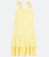 Vestido midi amarillo de algodón con tejido laise (ojales), escote cuadrado y tirantes ajustables con lazo. Presenta un diseño escalonado con volados en la falda.
