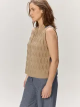 Chaleco de punto color beige con cierre frontal y patrón de rombos texturizados, sin mangas y con cuello redondo.