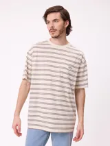 Remera de corte holgado con diseño de rayas horizontales en tonos beige, marrón y azul claro. Presenta cuello redondo, mangas cortas y un bolsillo frontal en el pecho con el logo de la marca bordado.