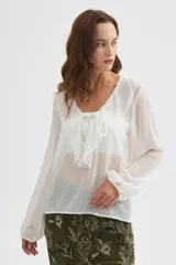 Blusa blanca de poliéster con cuello en V, volados frontales y mangas largas con elástico en los puños.