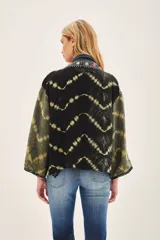 Kimono de estilo abierto con mangas amplias, confeccionado en viscosa con técnica de teñido tie-dye en tonos negro y verde oliva. Presenta una guarda frontal bordada con detalles de pedrería y apliques decorativos.