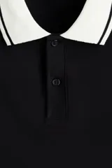 Polo de manga corta confeccionado en piqué de algodón, con cuello y bordes de mangas en color blanco con detalles de líneas negras. Presenta cierre frontal con botones y un corte ajustado.