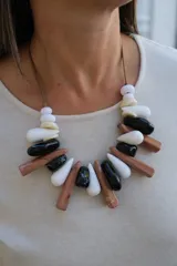 Collar de diseño artesanal compuesto por piezas de resina en forma de gotas y cilindros alargados en tonos blanco, negro y marrón, montadas sobre un cordón de hilo encerado.