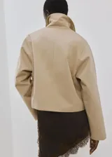 Chaqueta corta de algodón en color beige, con cuello camisero, mangas largas, dos bolsillos con solapa en el frente y cierre de botones.
