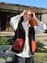 Chaleco negro con interior de corderito, con detalles en color naranja y ribeteado en marrón.