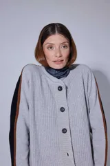 Saco de punto acanalado en color gris claro, con cierre frontal de botones oscuros. Presenta un diseño de bloques de color en las mangas, combinando negro y marrón, y un cuello redondo.