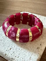 Brazalete elástico de diseño protagonista, compuesto por piezas rectangulares de acrílico en tono fucsia con efecto marmolado, intercaladas con eslabones metálicos dorados.