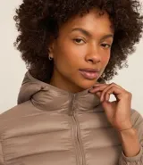 Campera puffer deportiva de mujer, confeccionada en tejido tecnológico ligero con relleno acolchado. Presenta capucha integrada, cierre frontal con cremallera y diseño de manga larga. La prenda destaca por su versatilidad, siendo capaz de transformarse en una pequeña cartera.