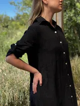 Vestido camisero largo de lino blanco, con cuello camisero, manga corta enrollada y cierre frontal de botones de nácar. Presenta aberturas laterales en el bajo.