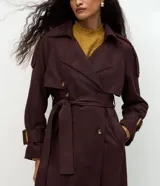 Trench coat largo de gamuza sintética con cuello peaked, cierre frontal cruzado con botones y cinturón ajustable en la cintura. Presenta mangas largas con reguladores en los puños y forro interior.
