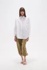 Camisa de algodón con diseño de rayas verticales, corte holgado, cuello camisero, cierre frontal con botones, mangas largas con puños y un bolsillo frontal con rayas horizontales.