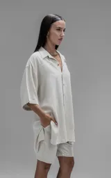 Camisa de corte oversize con cuello camisero, cierre frontal de botones y mangas cortas. Presenta un diseño holgado con bolsillos laterales integrados en la costura.