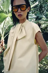 Camisa sin mangas confeccionada en algodón, con cuello redondo y detalle de lazada frontal. Presenta un diseño de corte holgado con bajo redondeado y cierre posterior mediante abertura y botones.