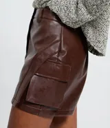 Short pollera marrón oscuro de poliuretano símil cuero, con diseño cruzado al frente, trabillas para cinto y bolsillos laterales estilo cargo.
