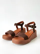 Sandalias de plataforma color chocolate con tira frontal ancha de gamuza y tira al tobillo con hebilla metálica ajustable.