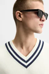 Chaleco de punto color crema con cuello en pico y ribete azul marino. Sin mangas y corte relajado.