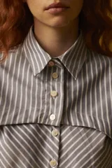 Camisa corta a rayas verticales grises y blancas, con cuello clásico, cierre frontal con botones y mangas largas con puños abotonados.