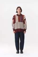 Buzo oversize de tejido de punto con diseño de bloques y rayas verticales en colores rojo, verde, bordó y crema. Presenta cuello alto tejido y terminaciones en rib en puños y ruedo.