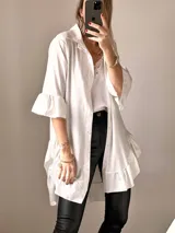 Camisa blanca de tejido suave tipo seda, con mangas tres cuartos y volados irregulares en mangas y ruedo. Tiene un largo ligeramente mayor en la espalda.