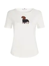 Remera de manga corta Tommy Hilfiger en color blanco, confeccionada en algodón regenerativo. Presenta un diseño clásico con cuello redondo y un estampado central distintivo de un perro salchicha con ropa.