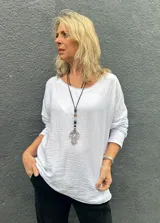 Blusa blanca de corte holgado y diseño minimalista, con cuello redondo y mangas largas. Presenta una textura sutilmente arrugada en la tela.