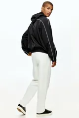Pantalón tipo jogger de corte sastrero, color blanco, confeccionado en tejido de punto de peso medio. Presenta pliegue cosido frontal, cintura elástica con cordón de ajuste, bolsillos laterales y bolsillo trasero insertado.