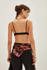 Crop top tipo bralette de encaje negro con detalles bordados y terminaciones delicadas. Presenta breteles finos y un diseño triangular que se ajusta al cuerpo.