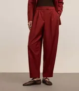 Pantalón de vestir color borgoña, de corte zanahoria, con pliegues delanteros, cierre con solapa y cremallera oculta.