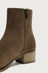 Bota corta de piel con acabado de serraje, diseño de horma cuadrada y tacón bloque de madera. Cuenta con cierre de cremallera lateral.