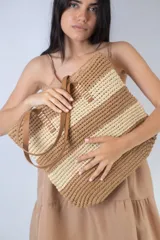 Bolso de playa tejido en rafia color beige con rayas horizontales negras y asas de cuero sintético marrón.