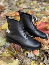 Botas de cuero de caña media, color marrón, con cordones frontales y suela track. Presentan un parche negro en la parte trasera del talón.