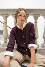 Cardigan de punto color beige con cuello redondo, cierre frontal con botones dorados, bolsillos frontales y terminaciones en crochet. Presenta hombreras internas y diseño de corte recto.