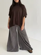 Poncho de tejido de punto color marrón chocolate, con cuello alto tipo polera y mangas cortas amplias. Presenta un diseño holgado con terminaciones acanaladas en el ruedo.