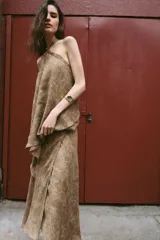 Falda midi de tiro alto y diseño asimétrico con cierre frontal cruzado y botón decorativo. Presenta una textura rústica con estampado sutil y forro interior marrón.