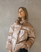 Campera puffer de corte oversize en tono champagne metalizado, con cuello alto envolvente y acabado brillante.